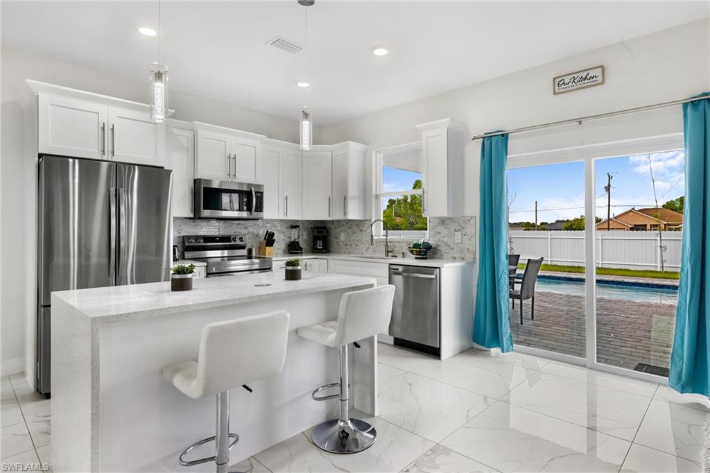 110 Nelson Road South Cape Coral, FL 33991 - Photo 7 of 27 a kitchen with granite countertop a refrigerator oven a sink a stove and chairs