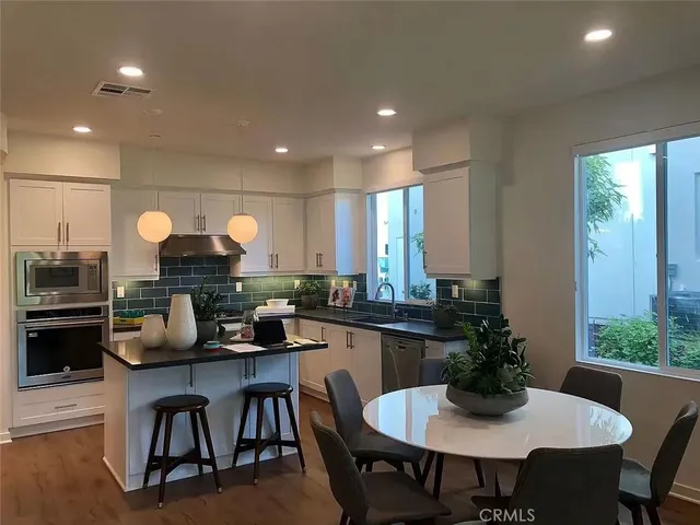 a kitchen with a dining table chairs and white cabinets with wooden floor