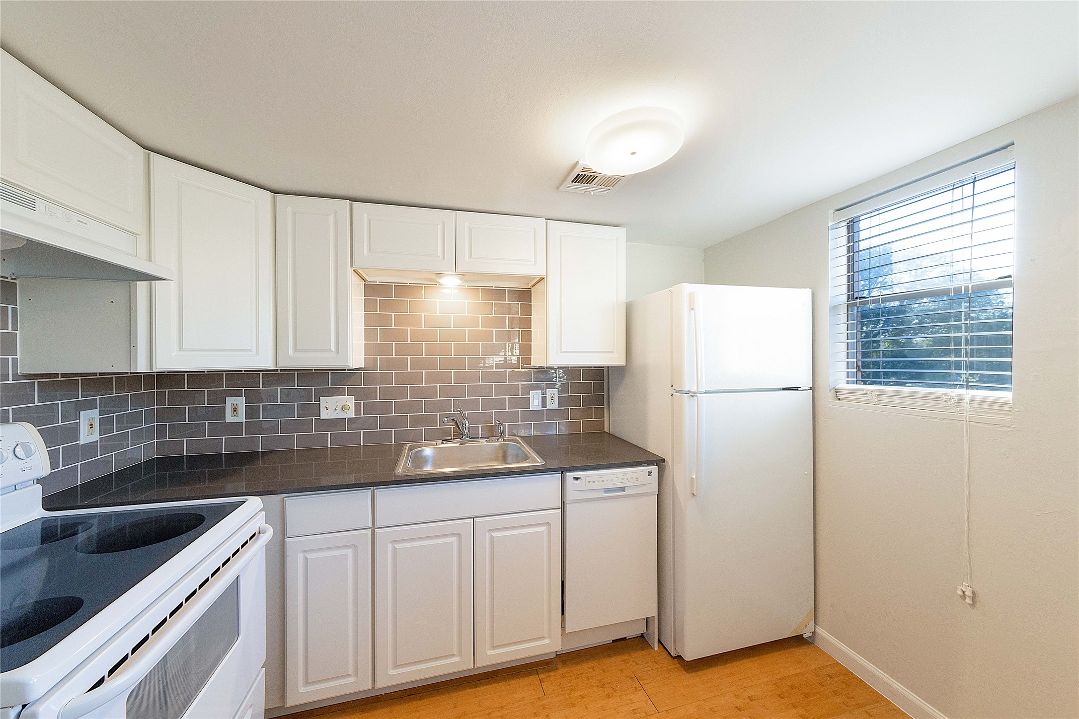 2500 Burleson Road, Unit 512 Austin, TX 78741 - Photo 10 of 16 Kitchen featuring white appliances, decorative backsplash, white cabinetry, dark countertops, and light wood finished floors