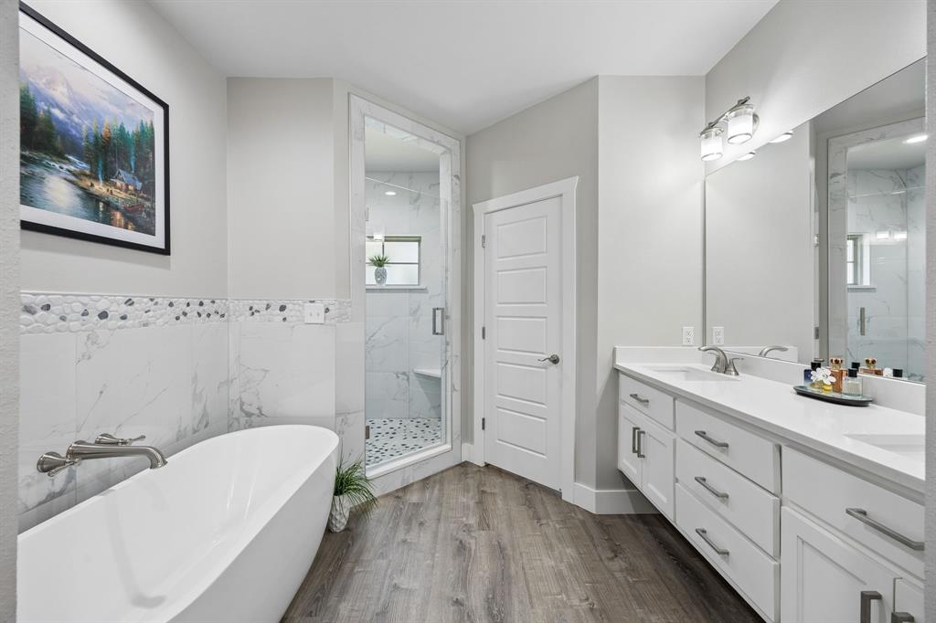 612 Frisco Road Sherman, TX 75090 - Photo 2 of 25 Bathroom featuring a freestanding soaking tub with brushed nickel fixtures, a large walk-in shower with glass enclosure and mosaic tile floor, a double vanity with stone countertops, and wood-finish flooring