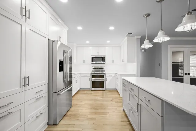 a white kitchen with granite countertop a refrigerator oven a sink dishwasher and white cabinets with wooden floor