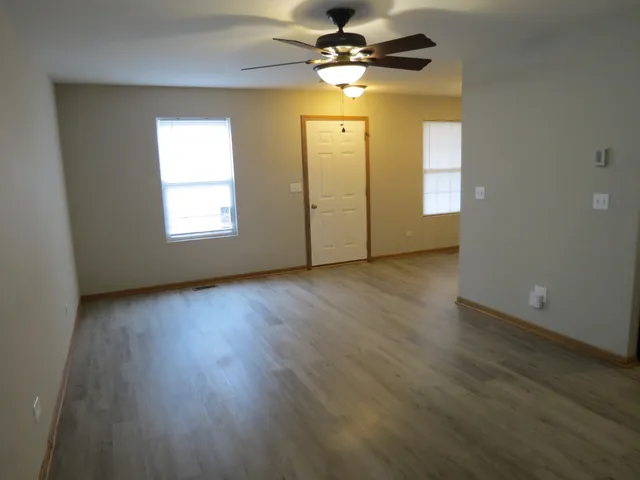 an empty room with wooden floor fan and windows