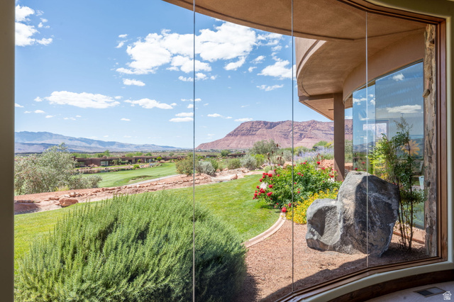 2331 West Entrada Trail, Unit 61 St. George, UT 84770 - Photo 27 of 69 Curved window wall featuring expansive desert landscaping, a manicured lawn, distant golf course, and red rock mountain backdrop