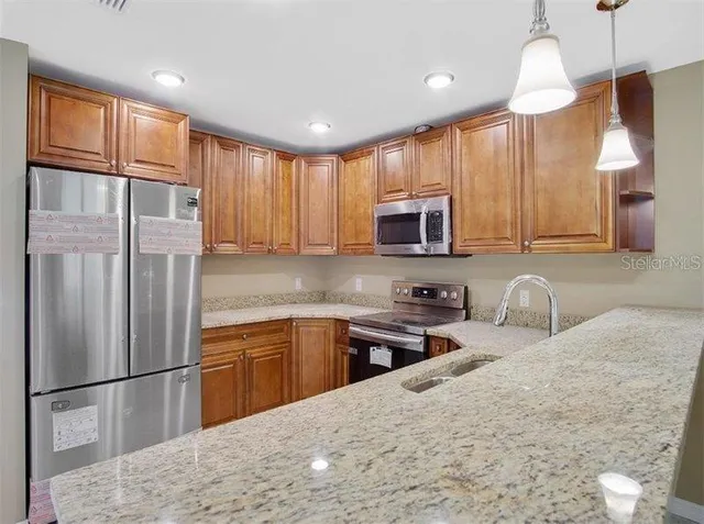 a kitchen with stainless steel appliances granite countertop a refrigerator a sink dishwasher a stove with wooden cabinets and floor