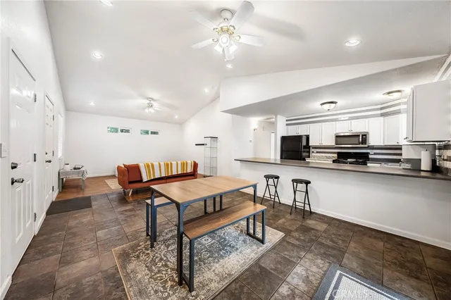 a living room with stainless steel appliances kitchen island a table chairs and a refrigerator