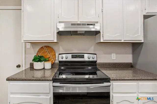 a kitchen with granite countertop a stove and white cabinets