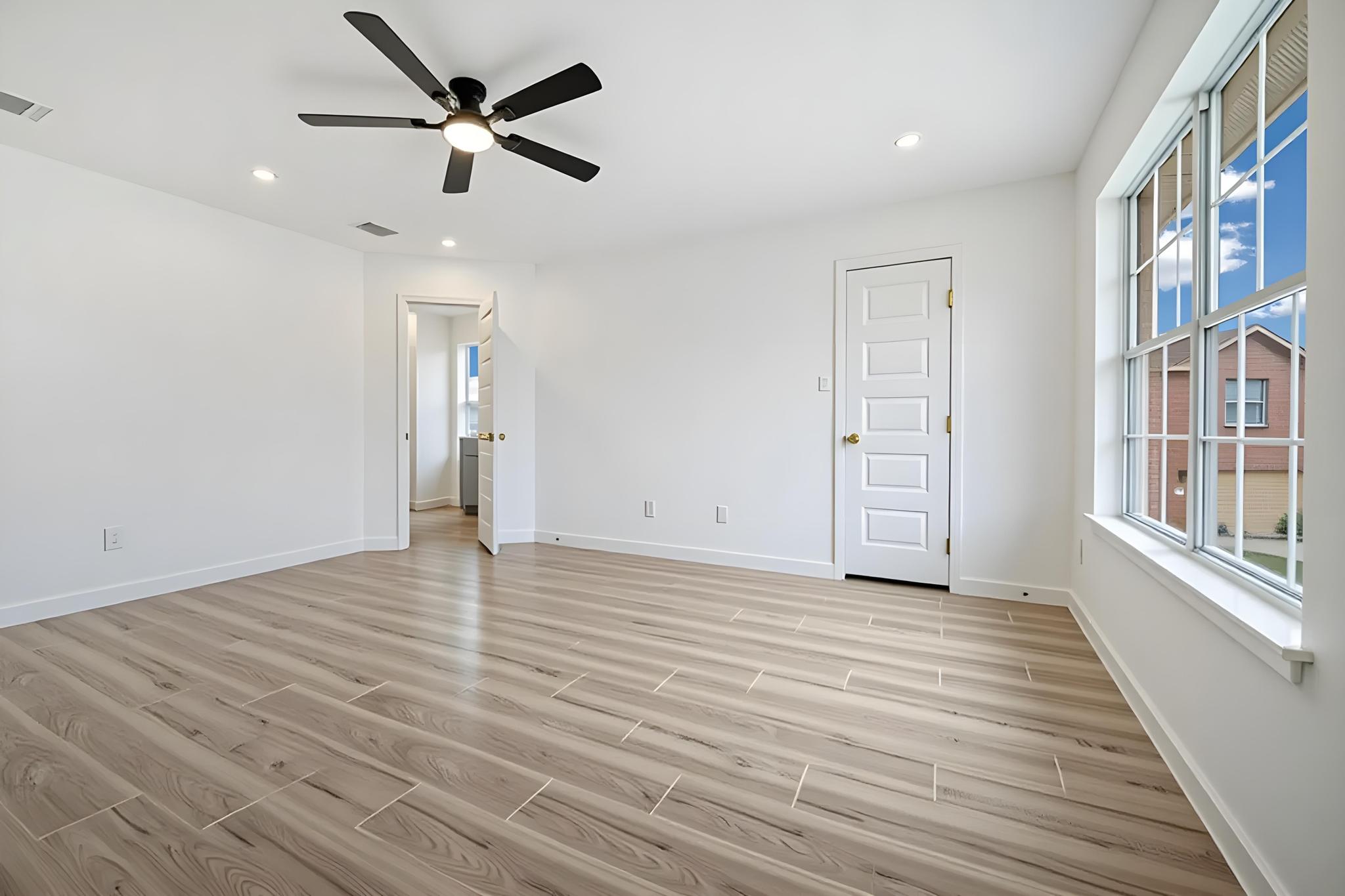 13501 Sierra Wind Lane Elgin, TX 78621 - Photo 17 of 19 Spacious room featuring wood-finish flooring, a contemporary ceiling fan, recessed lighting, a large window with grilles, and a paneled door