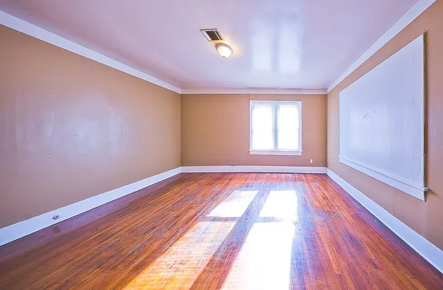 a view of an empty room with wooden floor and window