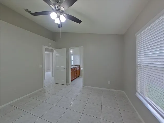en empty room with a chandelier fan and kitchen view