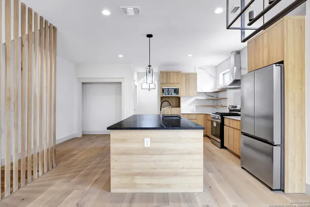 a kitchen with stainless steel appliances kitchen island granite countertop a refrigerator a stove and a sink with wooden floor