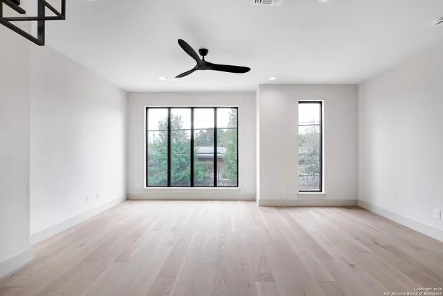 an empty room with wooden floor fan and windows