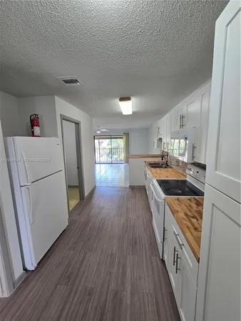 a kitchen with granite countertop a refrigerator a sink dishwasher a stove and white countertops with wooden floor