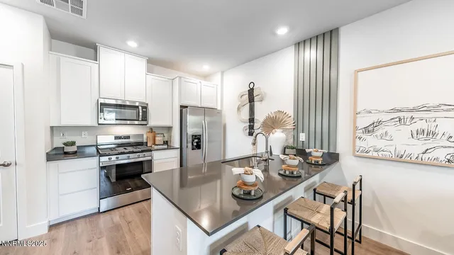 a kitchen with stainless steel appliances granite countertop a stove top oven a sink a refrigerator and white cabinets