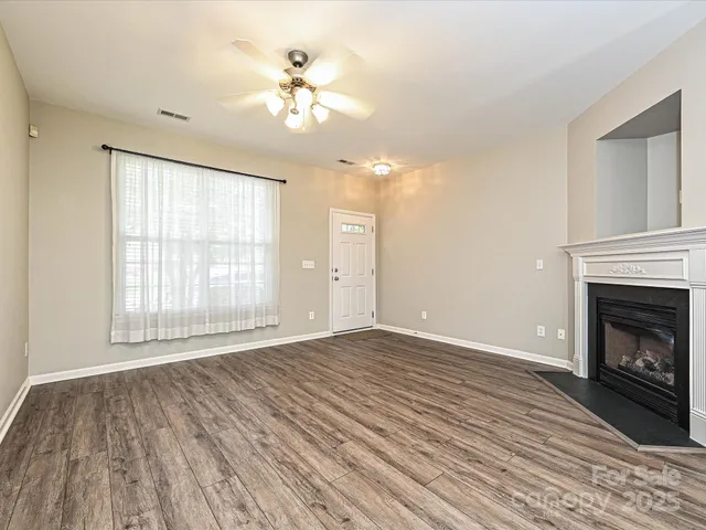 a view of an empty room with wooden floor fireplace and a window