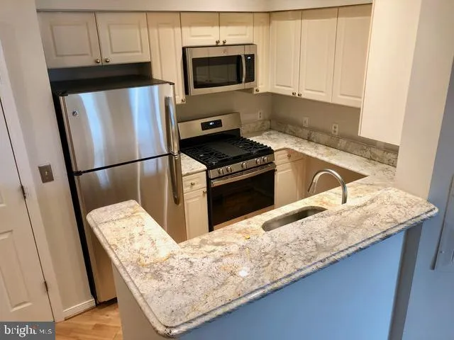a kitchen with granite countertop a refrigerator a stove and white cabinets