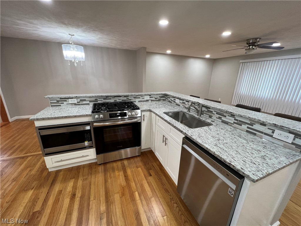 5105 Hillside Road Independence, OH 44131 - Photo 10 of 35 Kitchen with sink, light hardwood / wood-style floors, ceiling fan with notable chandelier, white cabinets, and appliances with stainless steel finishes