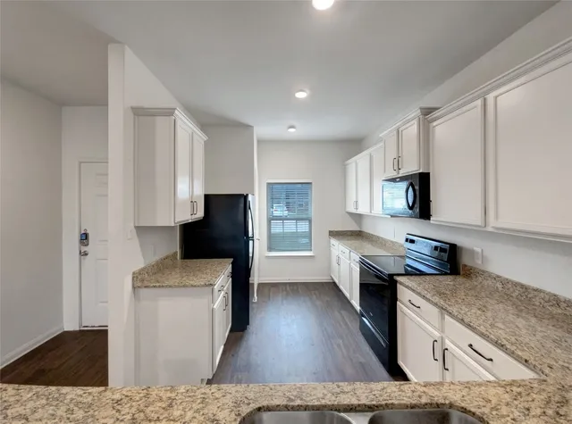 a kitchen with stainless steel appliances granite countertop a stove top oven a sink dishwasher and a refrigerator with wooden floor