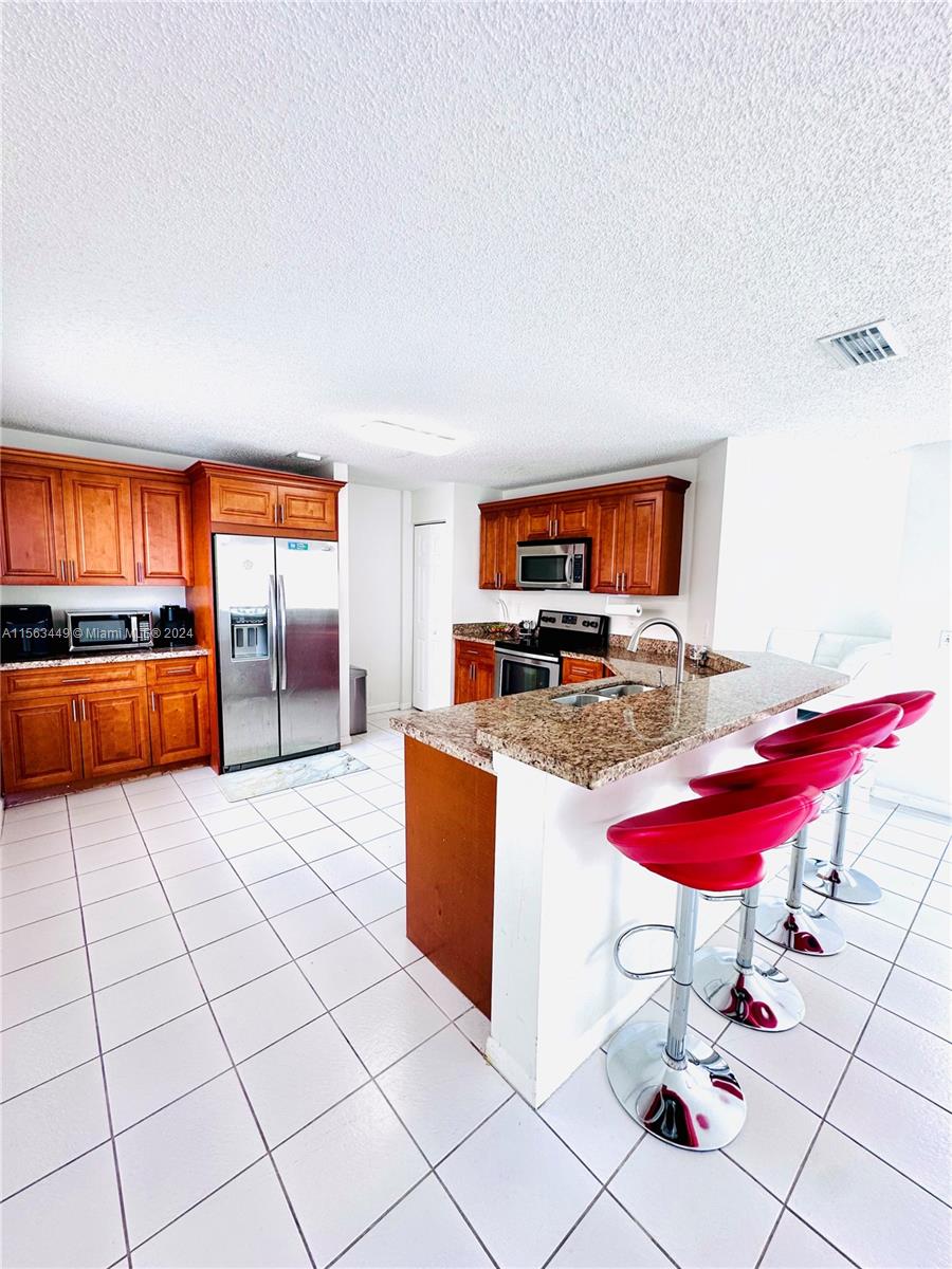 17456 Southwest 20th Street Miramar, FL 33029 - Photo 9 of 34 a kitchen with stainless steel appliances kitchen island granite countertop a refrigerator and a stove top oven