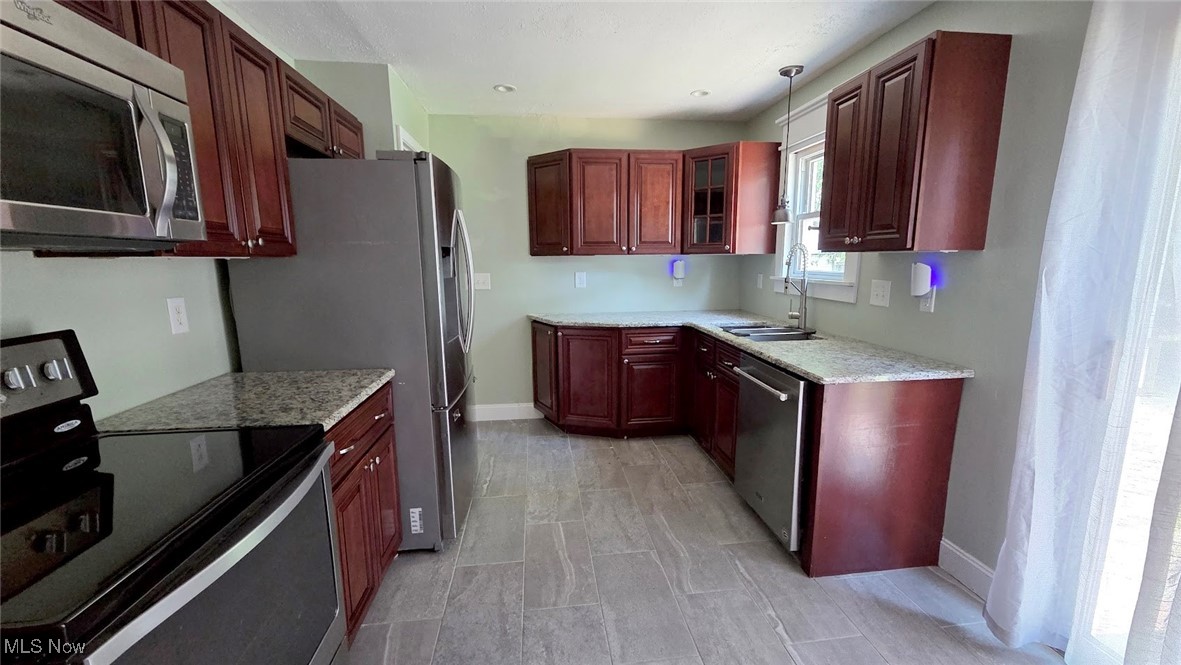 Kitchen with appliances with stainless steel finishes, glass insert cabinets, dark brown cabinets, and light stone counters