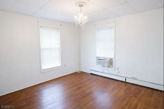 an empty room with wooden floor chandelier and windows