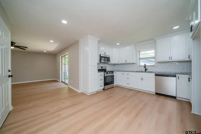 a large kitchen with stainless steel appliances granite countertop a stove a sink and white cabinets