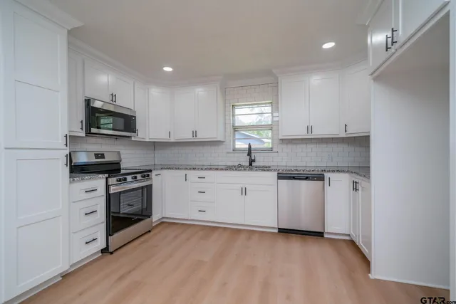 a kitchen with granite countertop white cabinets a stove a sink and a oven