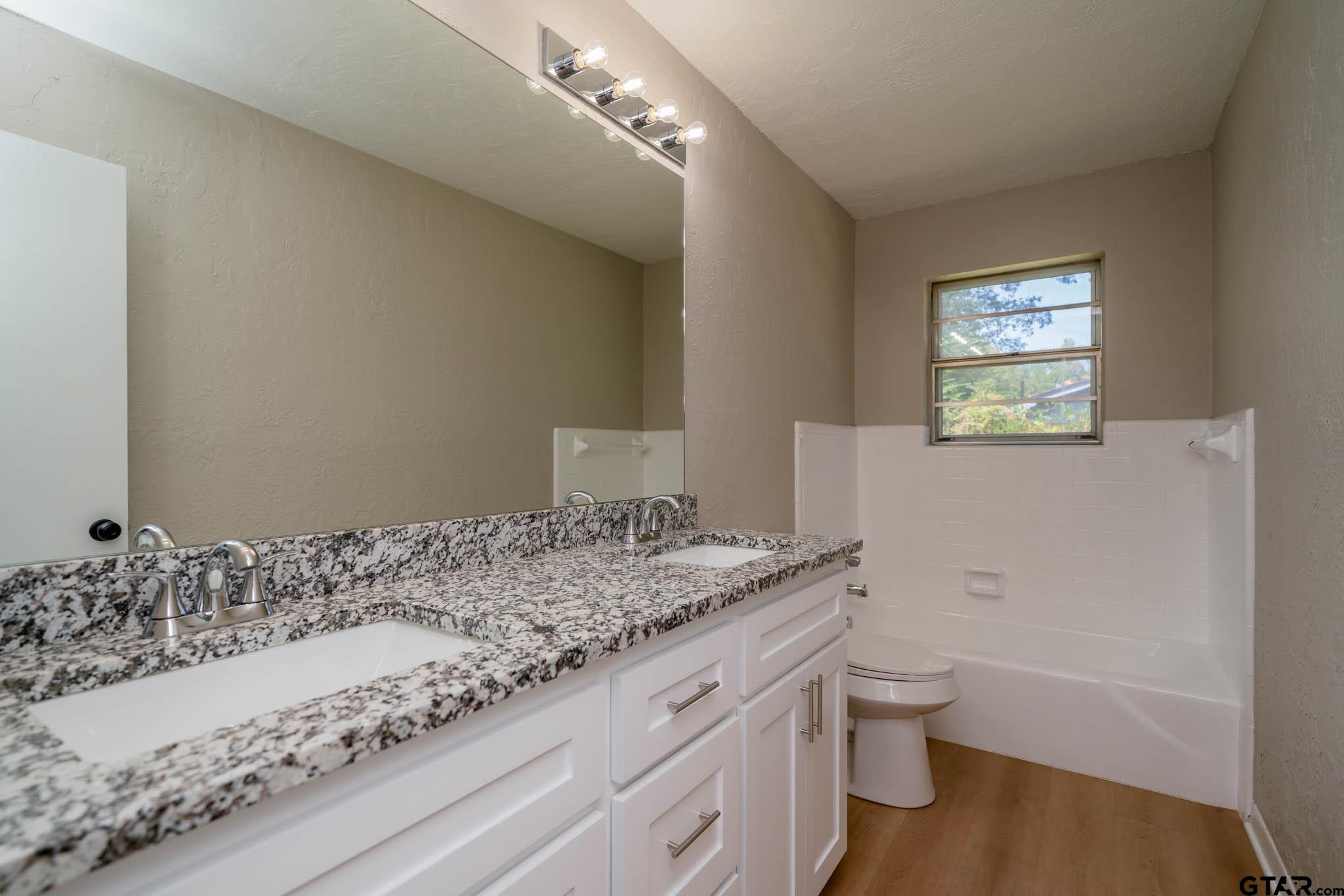 1411 Sapphire Street Longview, TX 75602 - Photo 31 of 38 a bathroom with a granite countertop sink a toilet and bathtub