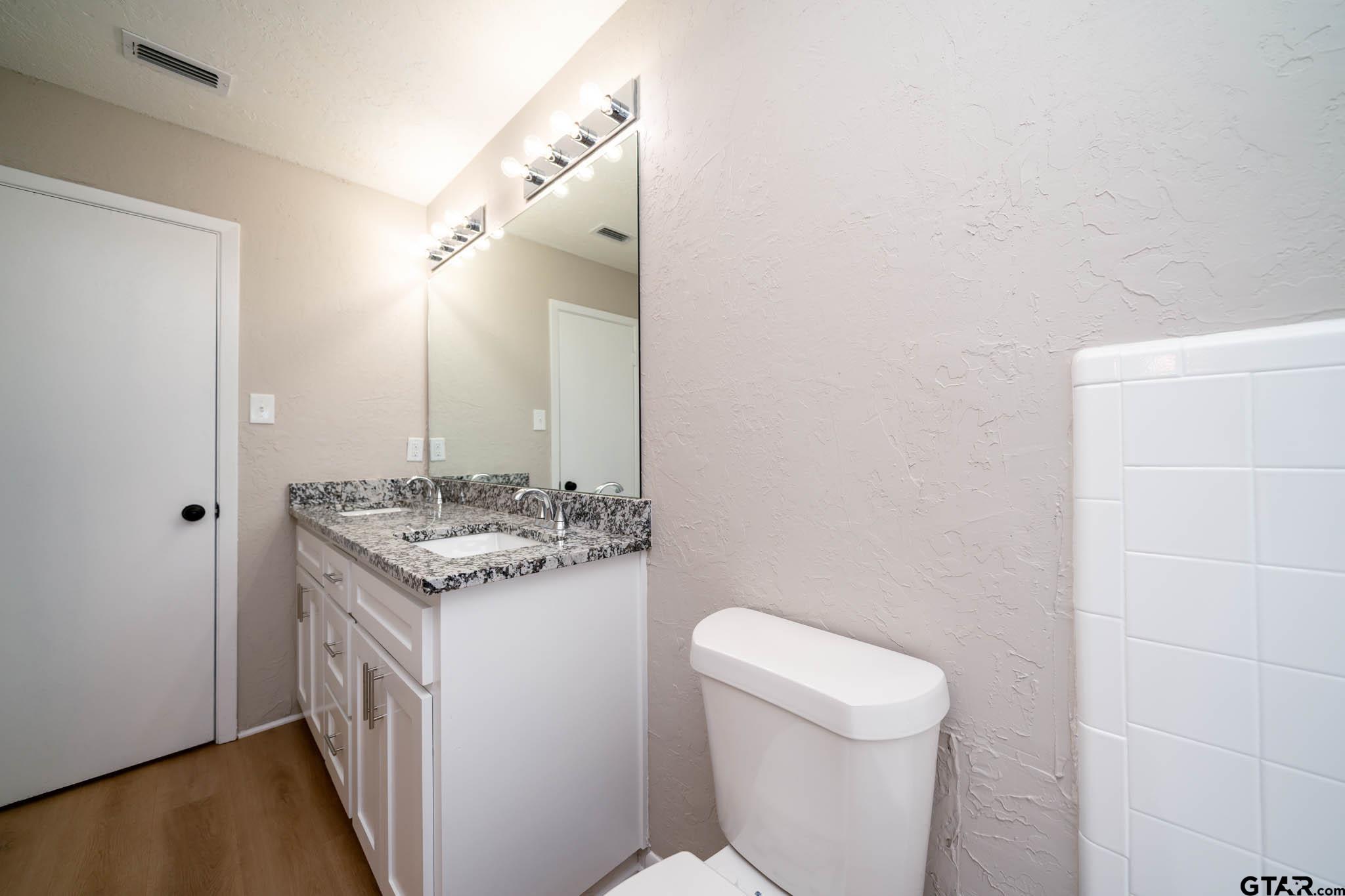 1411 Sapphire Street Longview, TX 75602 - Photo 32 of 38 a bathroom with a granite countertop sink a toilet and a mirror
