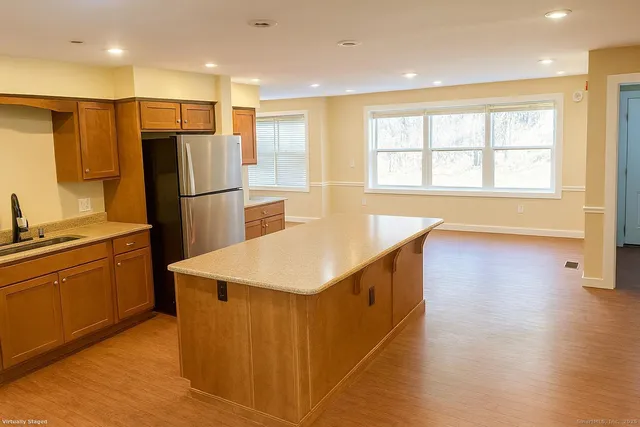 a kitchen with stainless steel appliances granite countertop a refrigerator a sink a stove and white cabinets with wooden floor