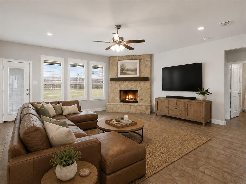 1601 Radecke Road Krum, TX 76249 - Photo 6 of 36 Spacious living area featuring a corner stone fireplace with a wood mantle, wood-finish flooring, a ceiling fan, and multiple windows