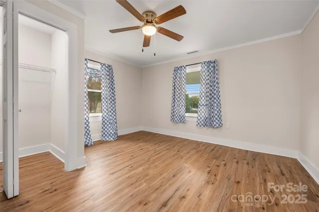 an empty room with wooden floor chandelier fan and windows