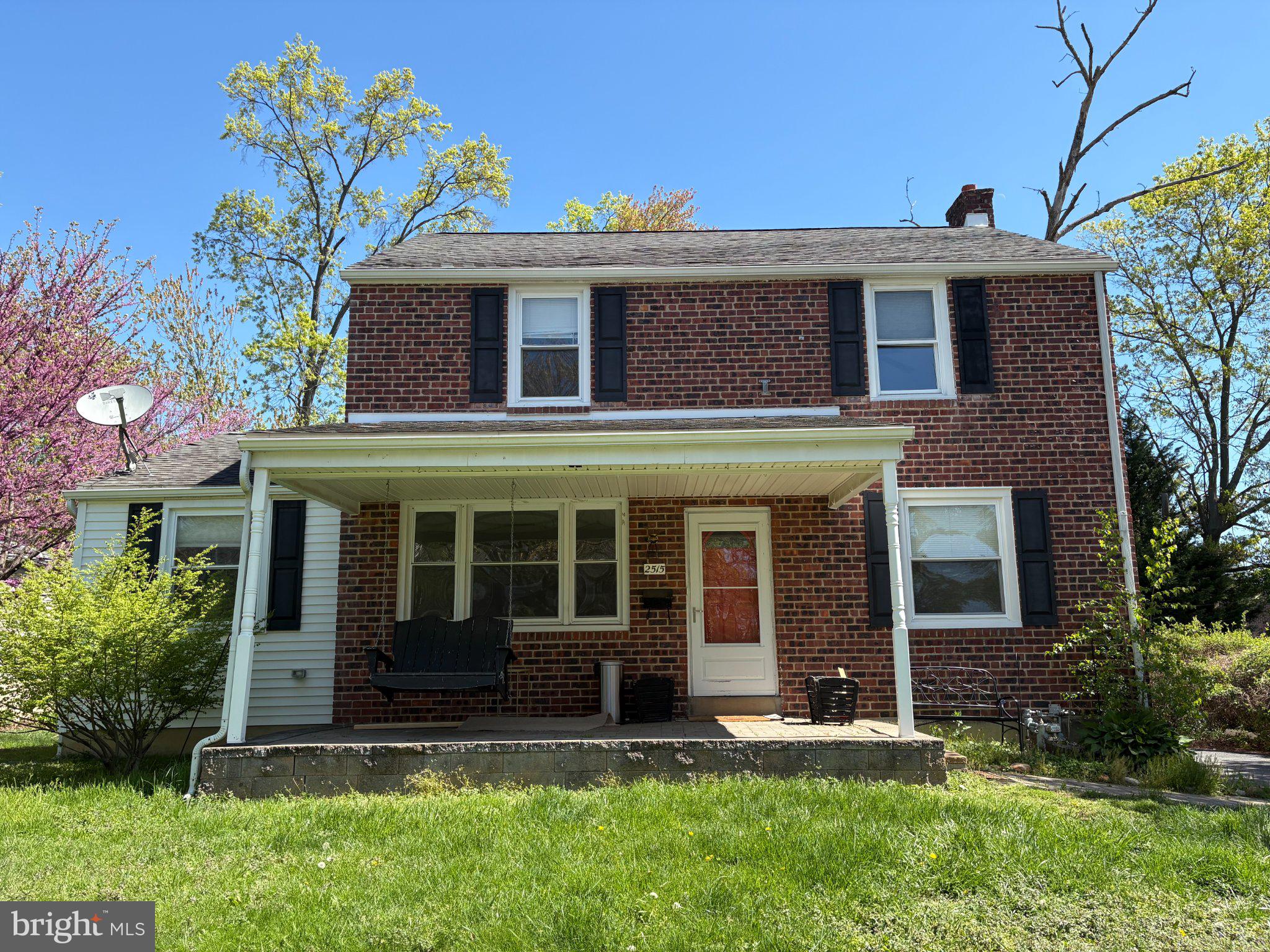 a view of a brick house with a yard plants and a large tree