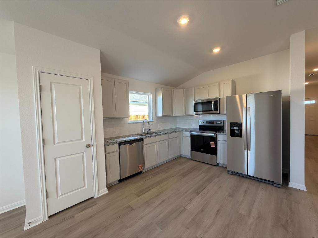 105 Honey Bee Road Jarrell, TX 76537 - Photo 7 of 9 Kitchen featuring stainless steel appliances, lofted ceiling, decorative backsplash, white cabinetry, and light wood-style floors