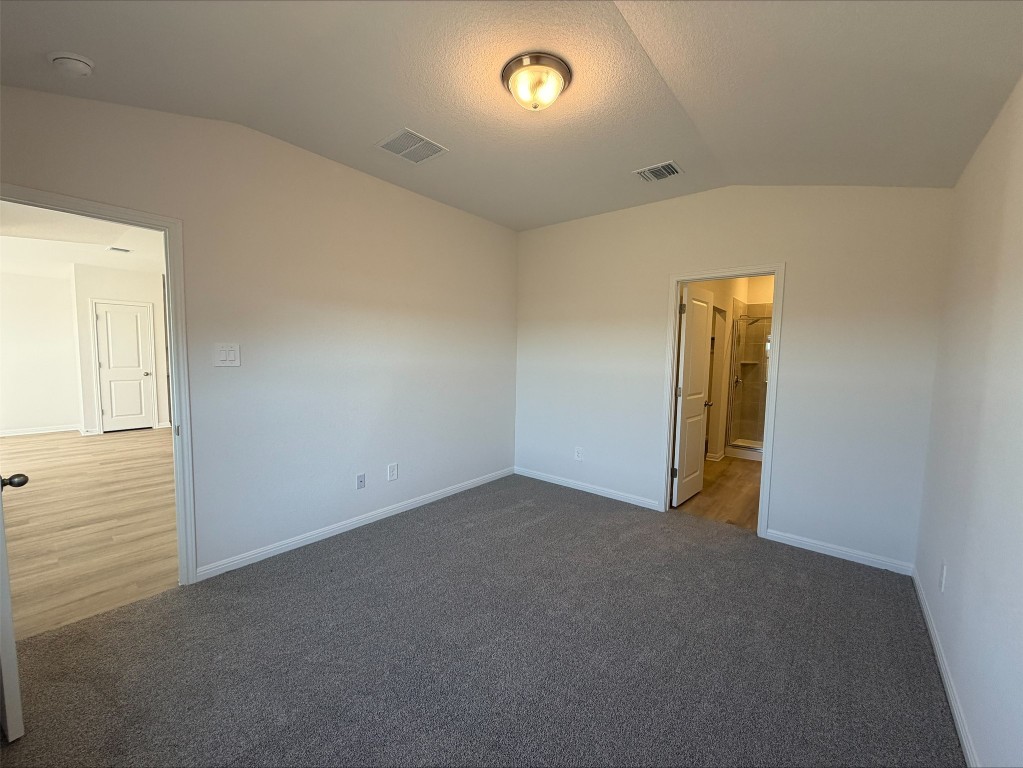 105 Honey Bee Road Jarrell, TX 76537 - Photo 8 of 9 Unfurnished bedroom with vaulted ceiling, carpet, ensuite bath, and a textured ceiling
