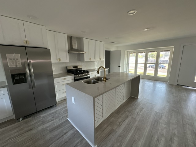 2101 Vanderbilt Lane Austin, TX 78723 - Photo 10 of 25 Kitchen featuring stainless steel appliances, white cabinets, decorative backsplash, light wood-style floors, and a kitchen island with sink