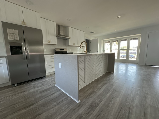 2101 Vanderbilt Lane Austin, TX 78723 - Photo 11 of 25 Kitchen featuring stainless steel fridge, white cabinetry, decorative backsplash, a kitchen island with sink, and dark wood-style flooring