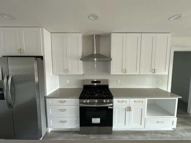 2101 Vanderbilt Lane Austin, TX 78723 - Photo 13 of 25 Kitchen featuring appliances with stainless steel finishes, white cabinets, backsplash, wall chimney range hood, and light wood-style floors