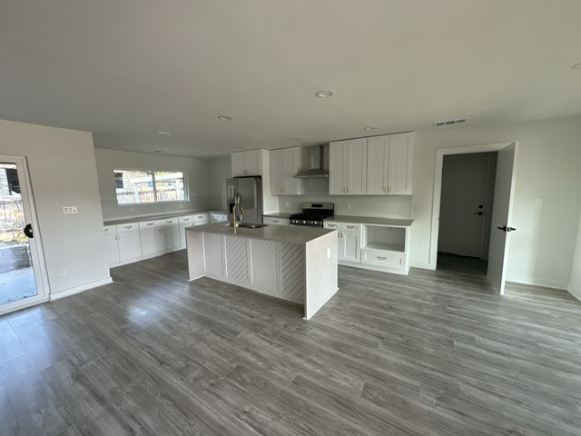 2101 Vanderbilt Lane Austin, TX 78723 - Photo 7 of 25 Kitchen featuring white cabinets, stainless steel appliances, wall chimney range hood, an island with sink, and dark wood-style flooring