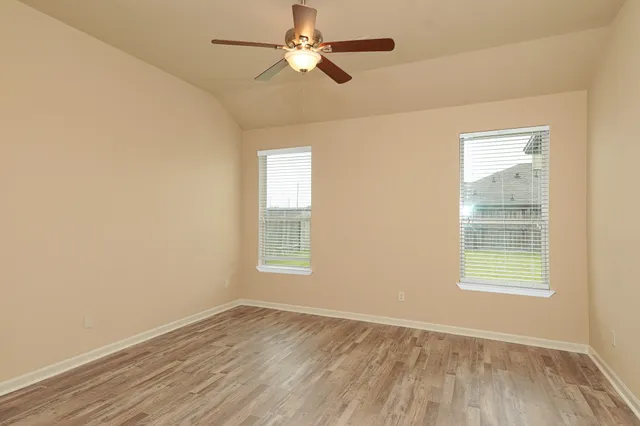 an empty room with wooden floor ceiling fan and windows