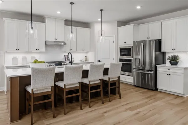 a kitchen with stainless steel appliances kitchen island granite countertop a table chairs microwave and white cabinets