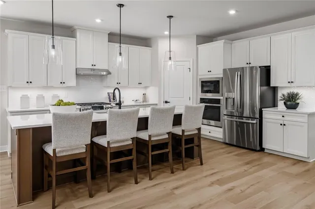 a kitchen with stainless steel appliances kitchen island granite countertop a table chairs microwave and white cabinets