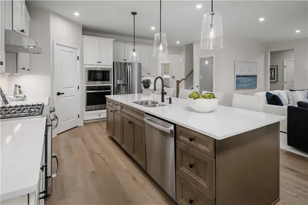 a kitchen with stainless steel appliances kitchen island granite countertop a refrigerator a sink dishwasher a oven and a dining table with wooden floor