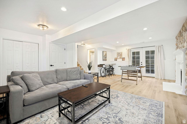 1723 Albury Road Sandy, UT 84092 - Photo 17 of 23 Spacious lower-level living area featuring light wood-finish flooring, recessed lighting, double French doors, a stone-clad fireplace with a white mantel, and bi-fold closet doors