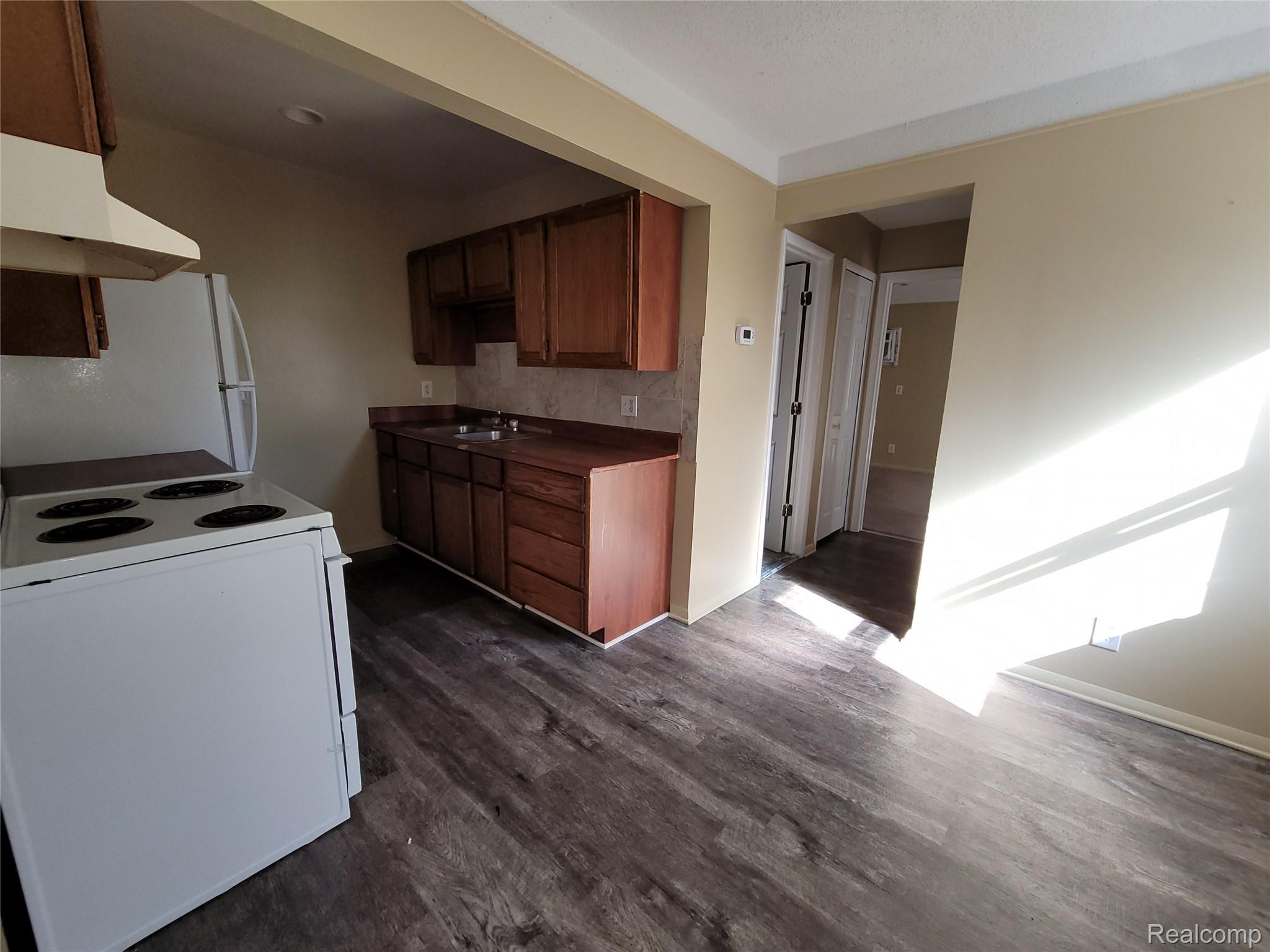Kitchen featuring white appliances, dark countertops, dark wood-style flooring, under cabinet range hood, and brown cabinetry