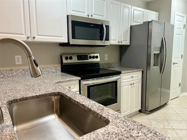 a kitchen with granite countertop a stove a microwave a refrigerator and cabinets
