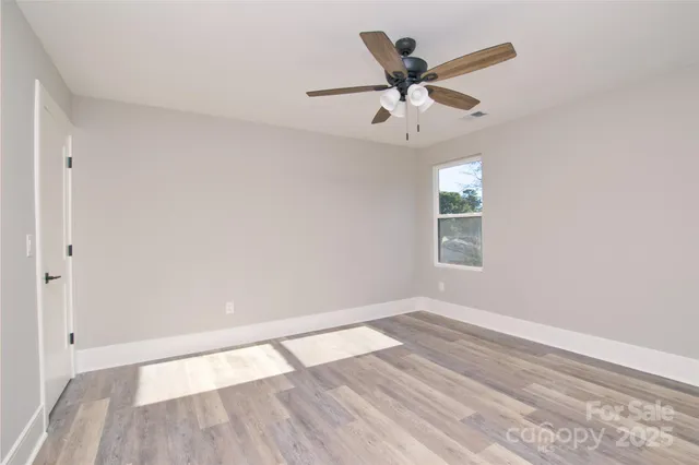 an empty room with wooden floor ceiling fan and windows