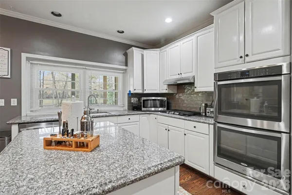 a kitchen with stainless steel appliances granite countertop a refrigerator oven a sink dishwasher a dining table and chairs with wooden floor