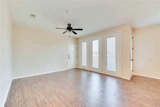 a view of an empty room with wooden floor and a ceiling fan