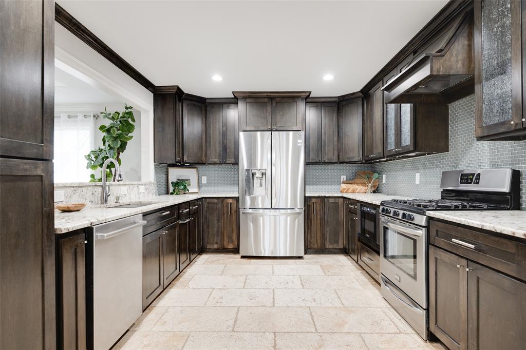 Kitchen featuring sink, appliances with stainless steel finishes, dark brown cabinetry, light stone countertops, and decorative backsplash