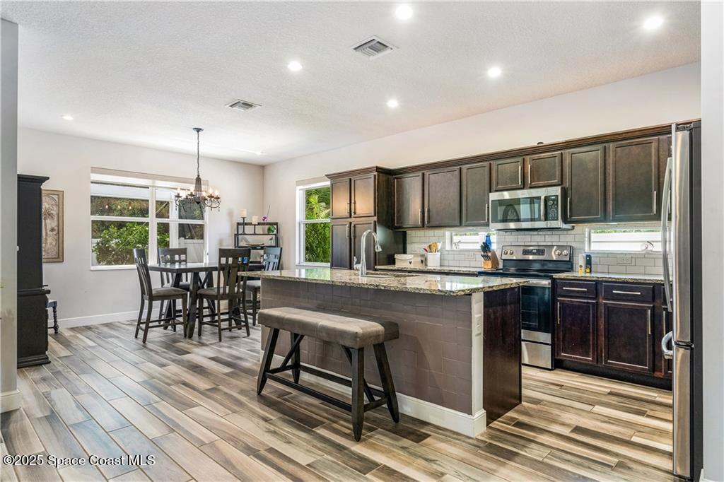 Undisclosed Address Vero Beach, FL 32966 - Photo 18 of 36 a kitchen with stainless steel appliances granite countertop wooden cabinets a refrigerator a stove a sink and a dining table with wooden floor